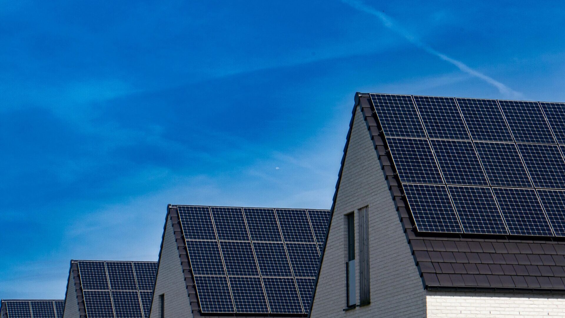 Hausdächer mit Photovoltaik-Anlagen vor einem blauen Himmel.